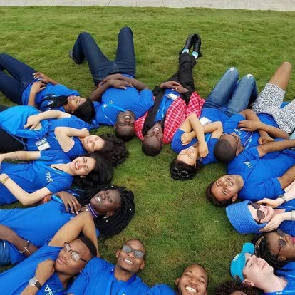 Kectil participants in blue shirts lying in a circle on the grass.