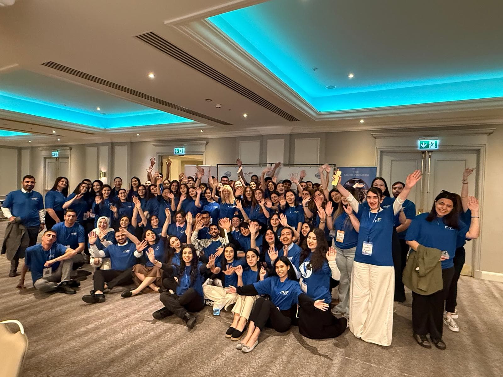 Kectil colleagues in blue program shirts waving together during a cohort gathering.